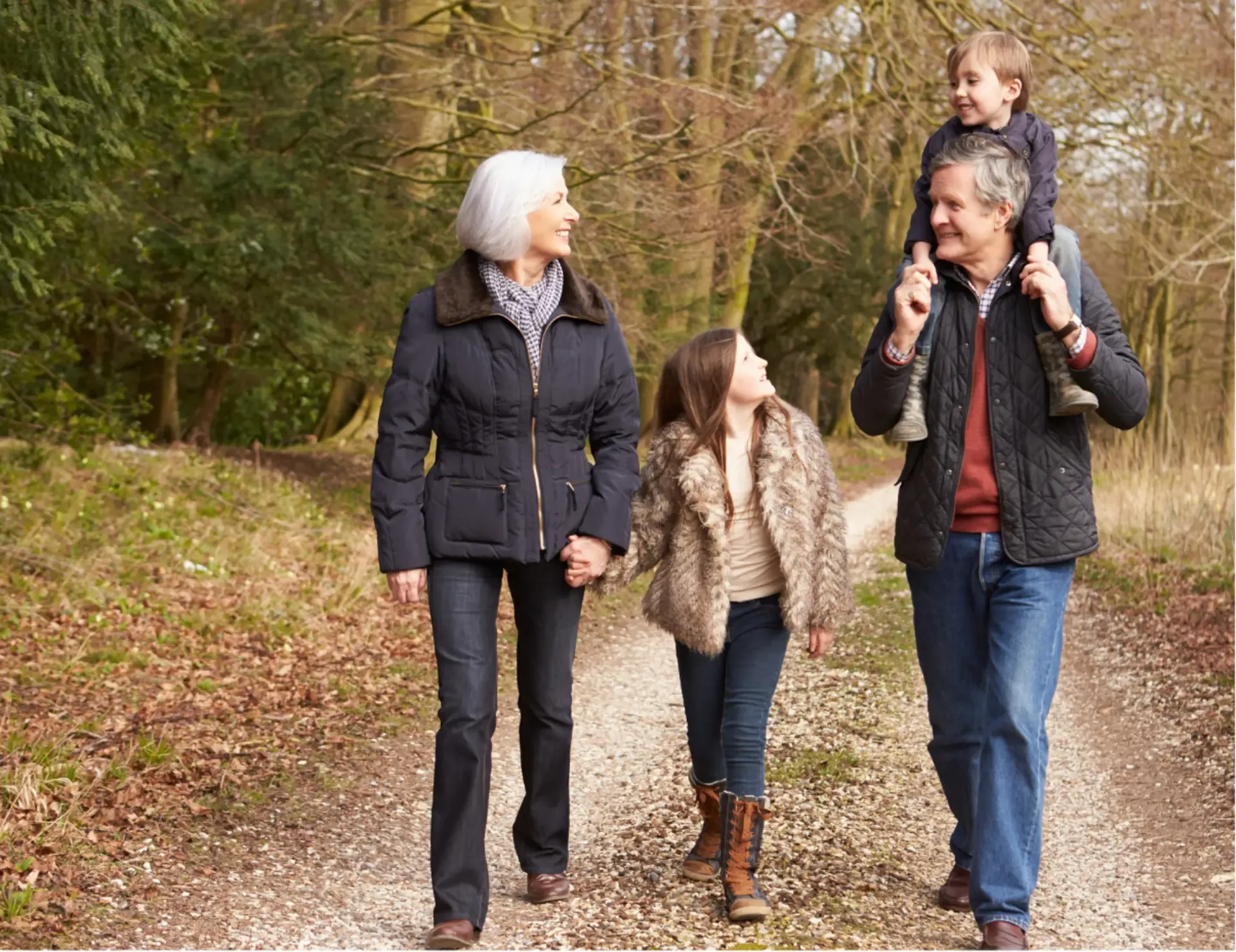 A family of four, including an older couple and their two children, strolls together down a tree-lined path